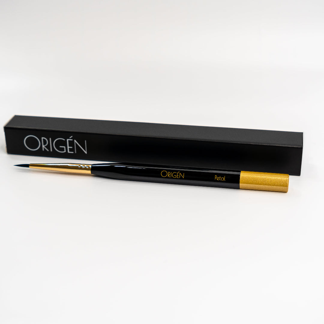 An ORIGÉN branded nail art petal brush with a gold-colored handle, displayed alongside its black packaging box.